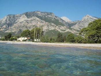 Scenic view of sea by mountains against clear blue sky