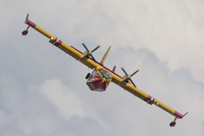 Low angle view of canadair plane flying against cloudy sky