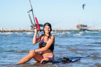 Full length of young woman sitting in sea against sky