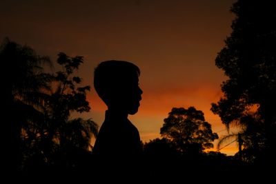 Silhouette boy standing by trees against sky during sunset