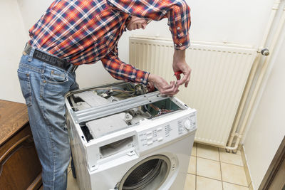 Middle aged man repairing broken washing machine with tools, household chores