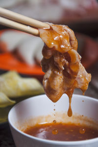 Close-up of chopsticks holding meat in soup bowl
