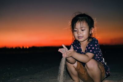 Girl looking away while sitting on land at sunset