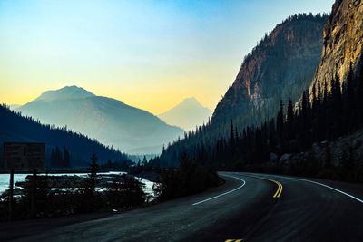 Road amidst trees and mountains against sky