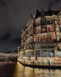 Illuminated buildings by river against sky at night