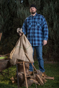 Portrait of lumberjack holding jute bag against trees at forest