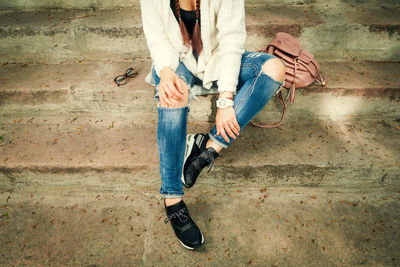 Fashionable young woman in a knitted cardigan and ripped jeans sits on the stairs. lifestyle