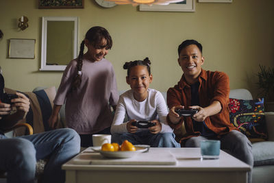 Portrait of happy gay couple playing video game with daughter while sitting on sofa at home