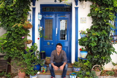 Portrait of smiling young man sitting at entrance of house