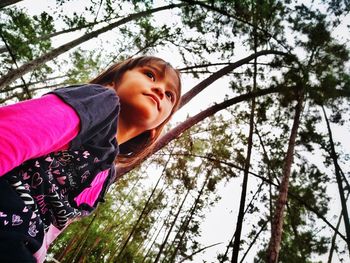 Low angle portrait of smiling girl against trees