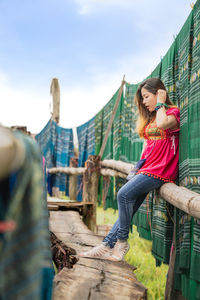 Side view of woman standing on retaining wall against sky