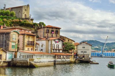 Buildings by river against sky