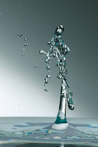 Close-up of drop falling on water against blue background