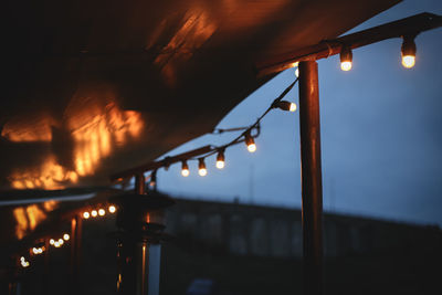 Illuminated light bulbs hanging against sky at night