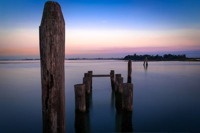 Wooden posts on sea against sky during sunset