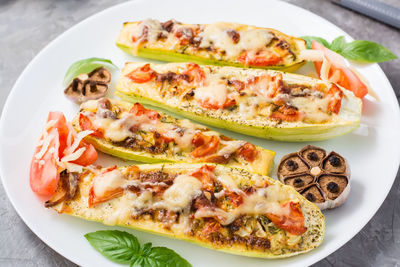 Ready-to-eat baked zucchini halves stuffed with cheese and tomato and basil leaves on a plate