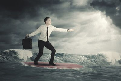 Digital composite image of businessman surfing in sea against cloudy sky