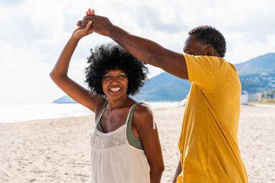 Young woman with arms raised standing at beach against sky