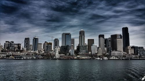 View of city at waterfront against cloudy sky