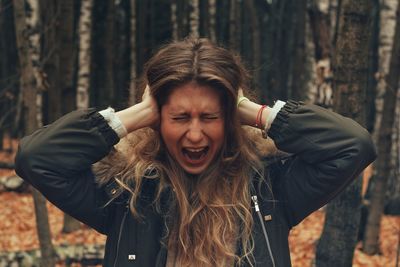 Young woman screaming while covering ears in forest