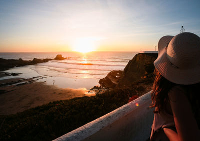 Rear view of woman standing on beach against sky during sunset