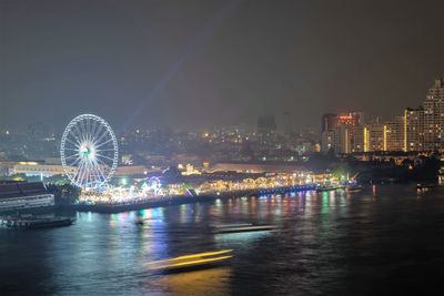 Illuminated ferris wheel in city against sky at night