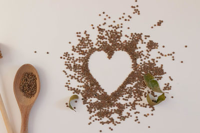 Heart made of raw lentils on a white background with kitchen utensils such as wooden spoon. 