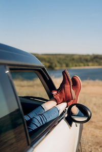 Low section of woman resting legs on car door against road