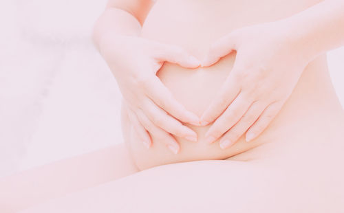 Midsection of pregnant woman making heart shape with hands on stomach