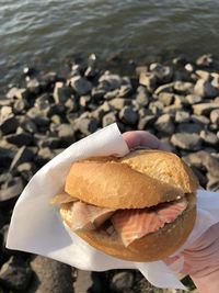 Cropped hand holding burger at beach