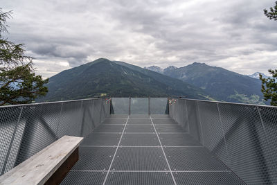 Footbridge leading towards mountains against sky