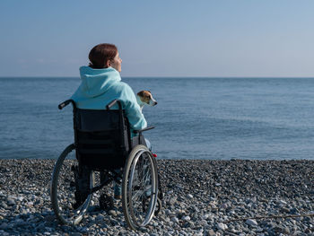 Rear view of woman sitting on wheelchair at beach