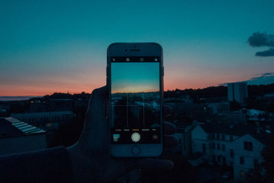 Man using mobile phone against buildings in city at sunset