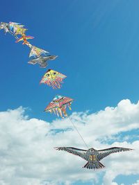 Low angle view of kites flying against blue sky during sunny day
