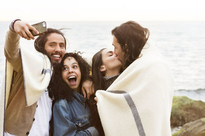 Friends clicking selfie at beach against sea