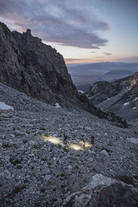 Three hikers with headlamps hike through the dawn in the tetons