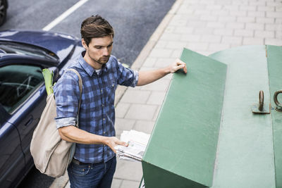 Young man putting newspaper in recycling bin