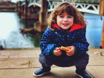 Portrait of smiling girl crouching against river in city