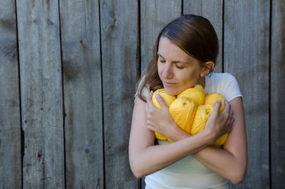 Woman holding yellow wool against wooden wall