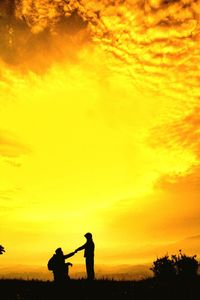 Silhouette men standing against orange sky