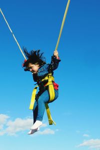 Low angle view of girl bungee jumping against blue sky