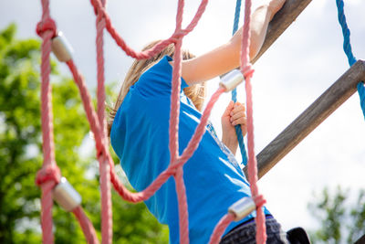 Close-up of child holding rope in playground against sky