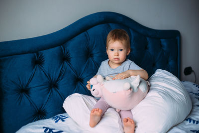 Funny little child is having fun, playing with soft toys on the couch at home.