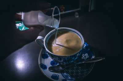 Close-up of hand pouring milk in tea on table