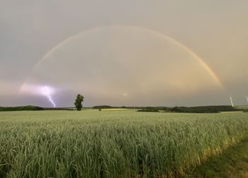 Scenic view of agricultural field against sky with a rainbow and a lightning 
