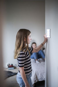 Girl using digital tablet on wall with sister in background at smart home