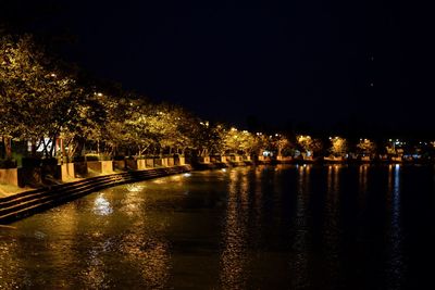 Illuminated city by river against sky at night