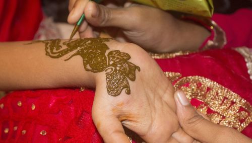 Midsection of woman making henna tattoo on hand