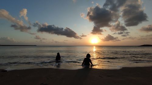 Silhouette people at beach against sky during sunset