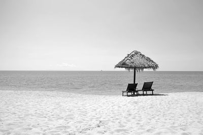 Empty chairs with thatched roof at beach against clear sky during sunny day